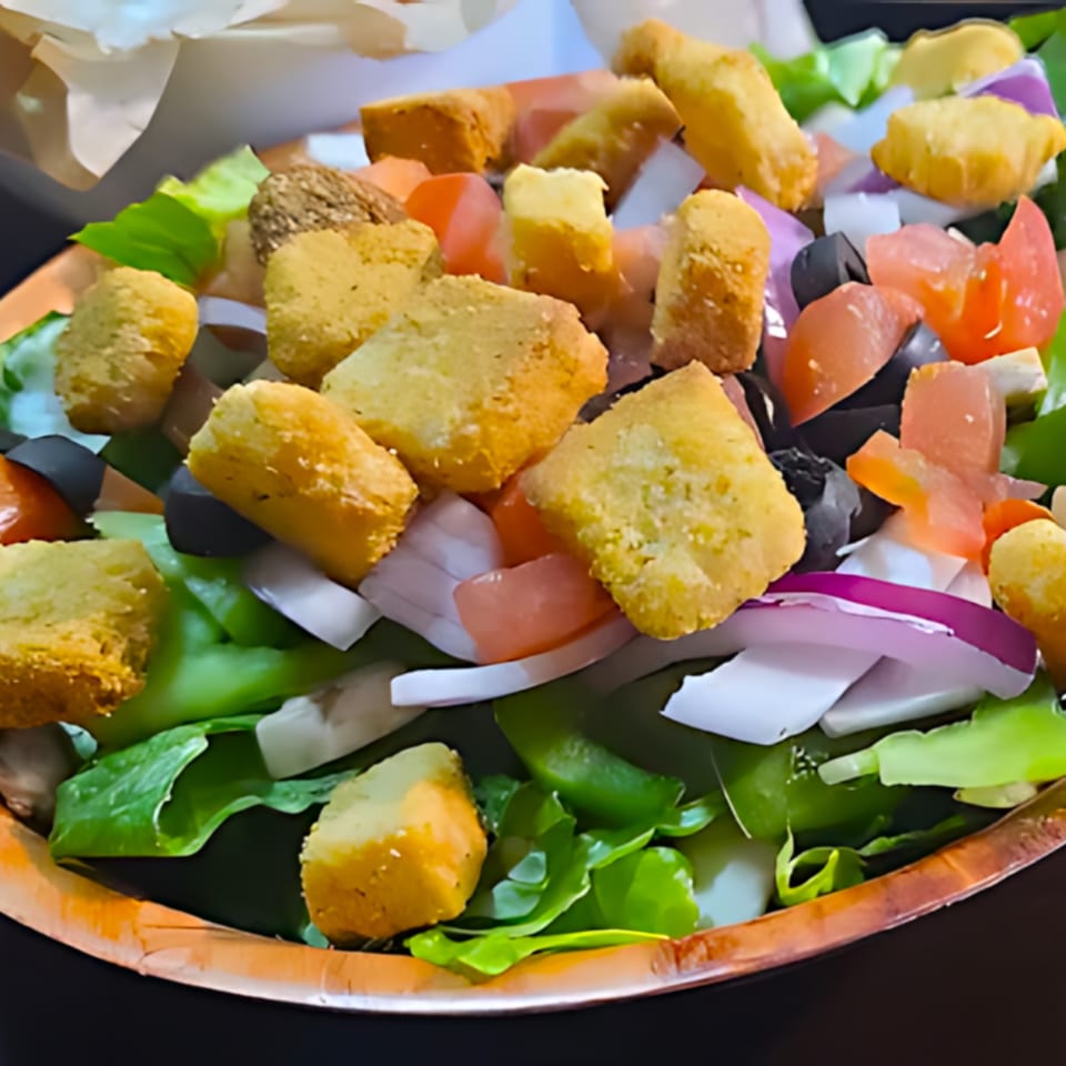 A fresh salad with lettuce, tomatoes, black olives, red onions, and croutons in a bowl.