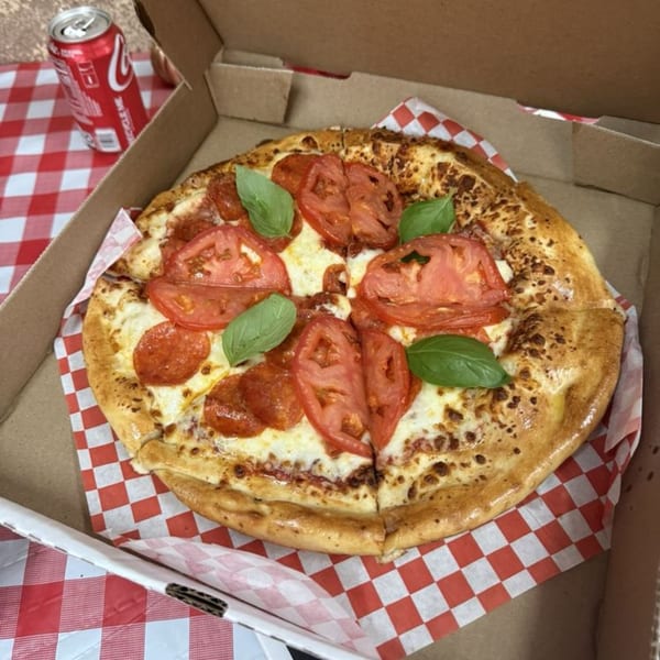 Gezziny's pepperoni and tomato pizza with basil in a box, next to a Coca-Cola can.