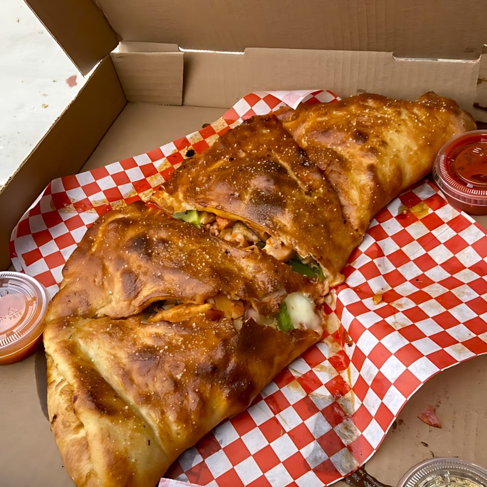 A large, golden-brown calzone from Gezziny's Homemade Pizza, sliced open in a box with red-and-white checkered paper.