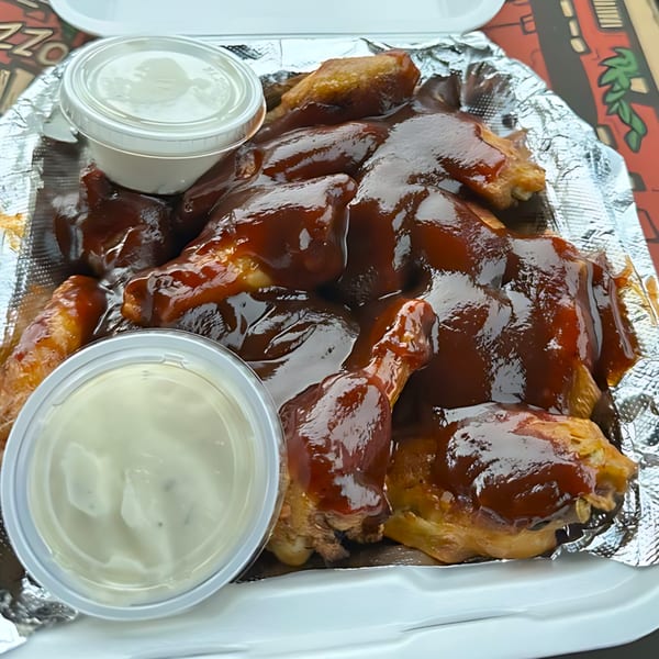 Gezziny's BBQ chicken wings in a foil-lined container with two cups of dipping sauce.