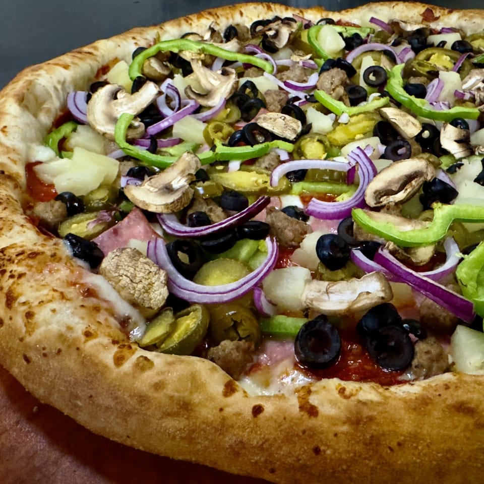 Close-up of a loaded pizza with mushrooms, olives, peppers, onions, and pineapple.