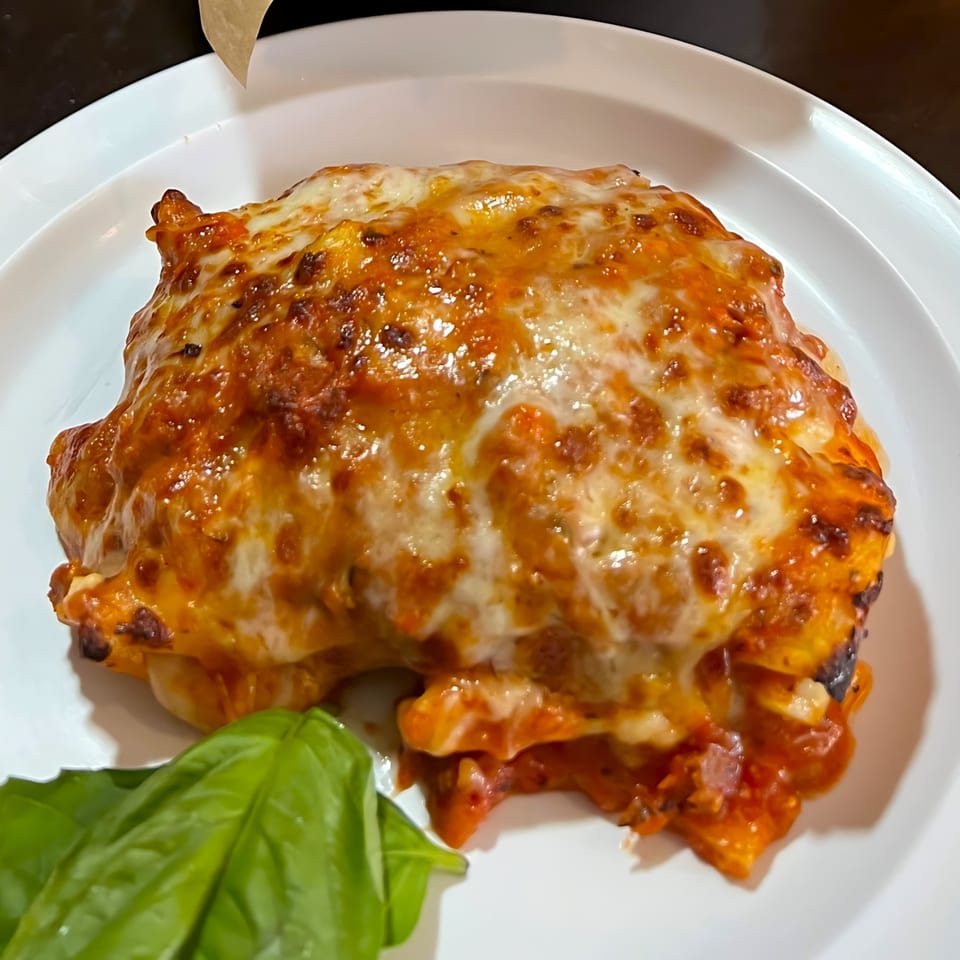 A serving of lasagna with melted cheese and tomato sauce, garnished with fresh basil on a white plate.
