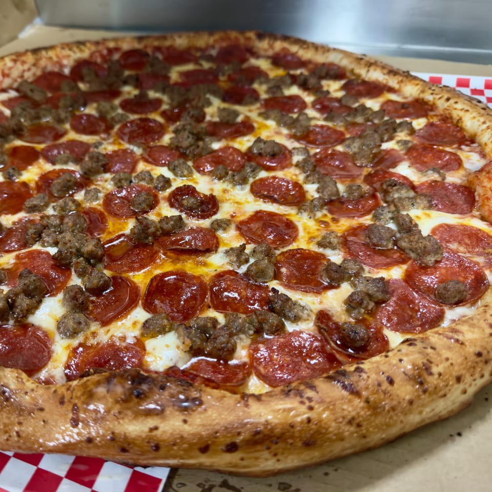 Close-up of a pepperoni and sausage pizza with melted cheese and a golden-brown crust.